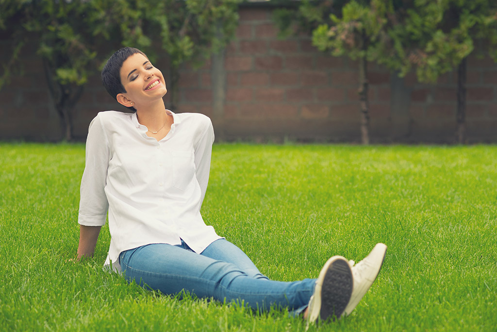 Beautiful smiling girl sitting on the grass of home garden on su